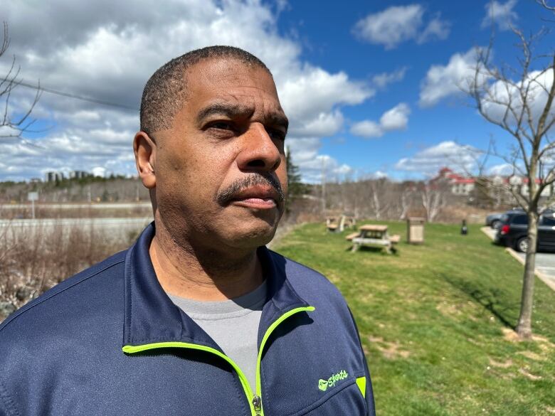 A man is shown looking beyond the camera in a blue tracksuit on a sunny day.