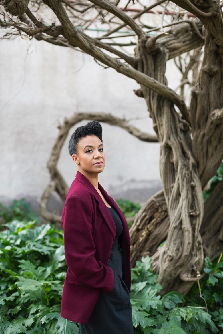 A woman stands beside a twisty tree.