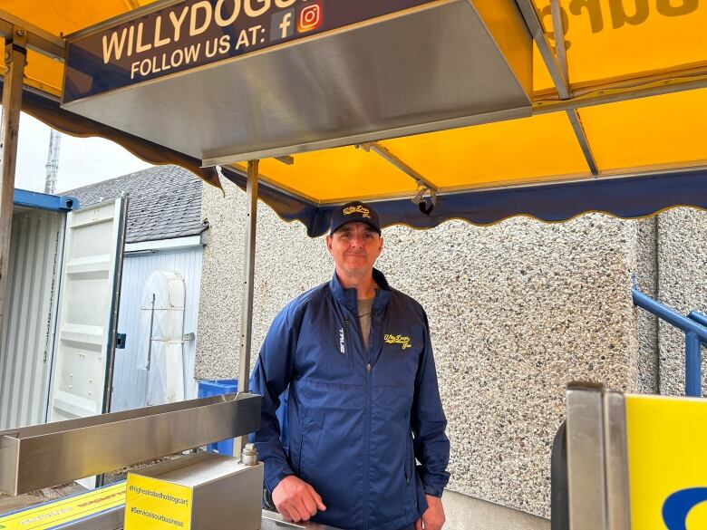 A man stands in front of a hot dog cart. 