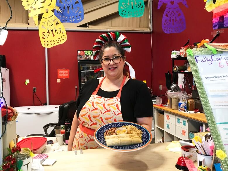 A woman holding a plate of tamales, stands behind a counter.