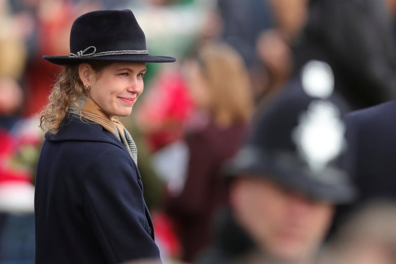 A person wearing a hat stands in front of a line of people.