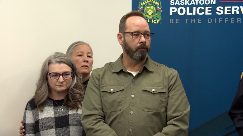 Three people stand listening.