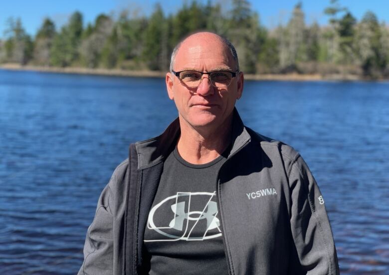 A man with glasses stands by  a lake.