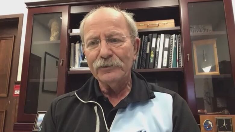 An elderly man with glasses is pictured wearing a black and blue athletic top.