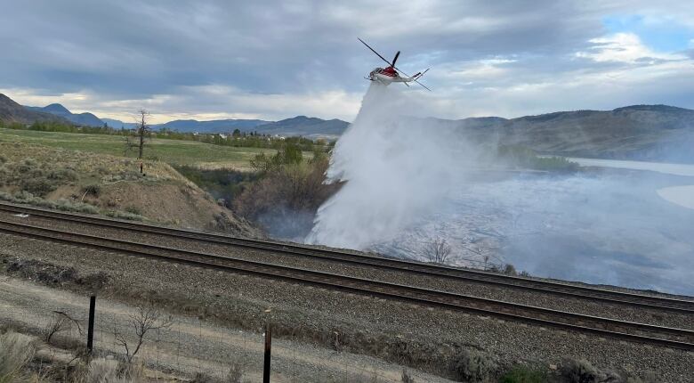 A helicopter sprays water on a patch of grass near a railway track.