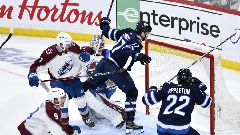 A hockey player moves towards the net while surrounded by players in the other team.