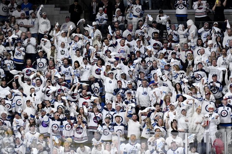 Rows of people standing up at a hockey arena, all wearing white outfits.