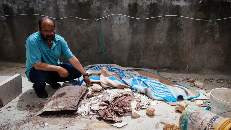 A man kneels over a pillow soaked with dried blood.