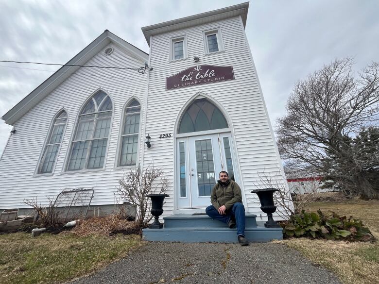 Man sitting on steps of large white building.