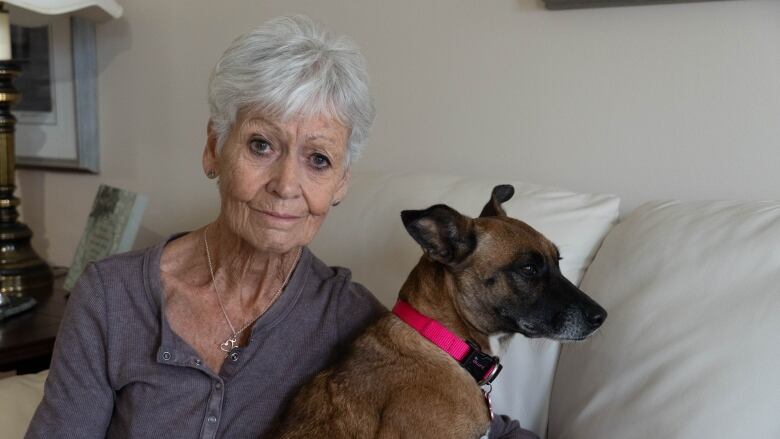 A woman sits on the couch with a dog at her side. 