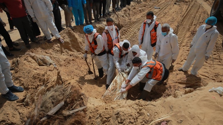 Workers wearing white hazmat suits used shovels to dig around buried bodies wrapped in white bags.