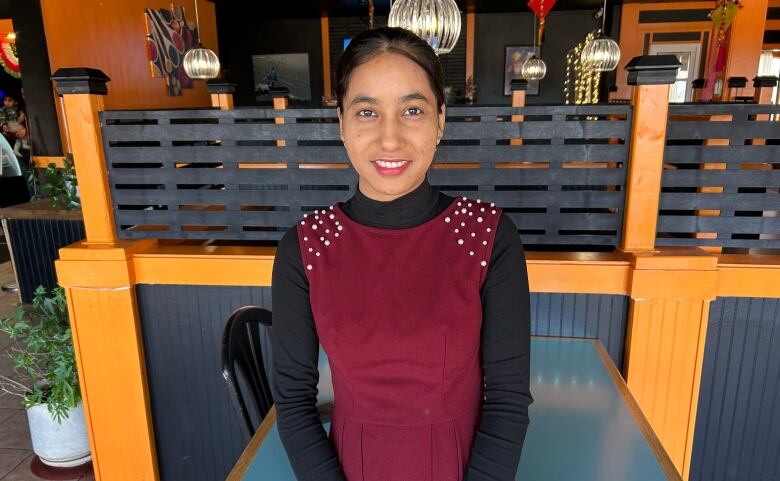 Smiling woman in burgundy smock and black turtleneck stands in restaurant. 