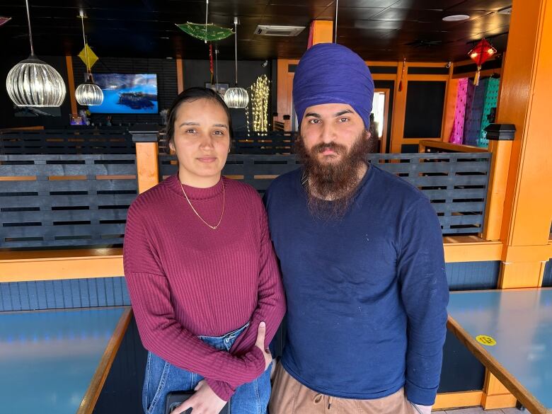 Woman in a burgundy sweater and man in a blue turban and shirt stand in a restaurant.