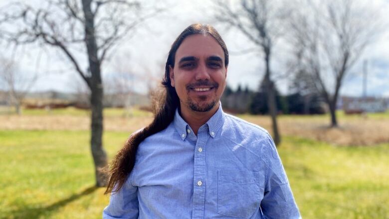 A man with long dark hair looks into the camera.