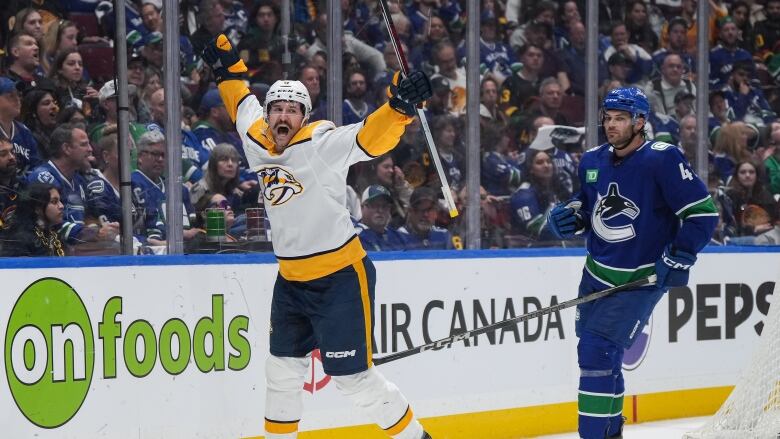 A hockey player wearing yellow and white celebrates as a player wearing blue grimaces.