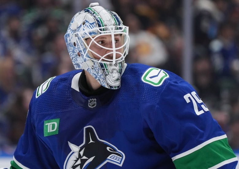 A hockey goalie with a blue and white helmet looks on.