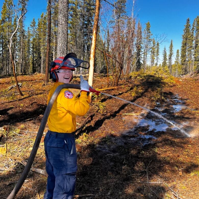 A firefighter holding a hose and smiling. 