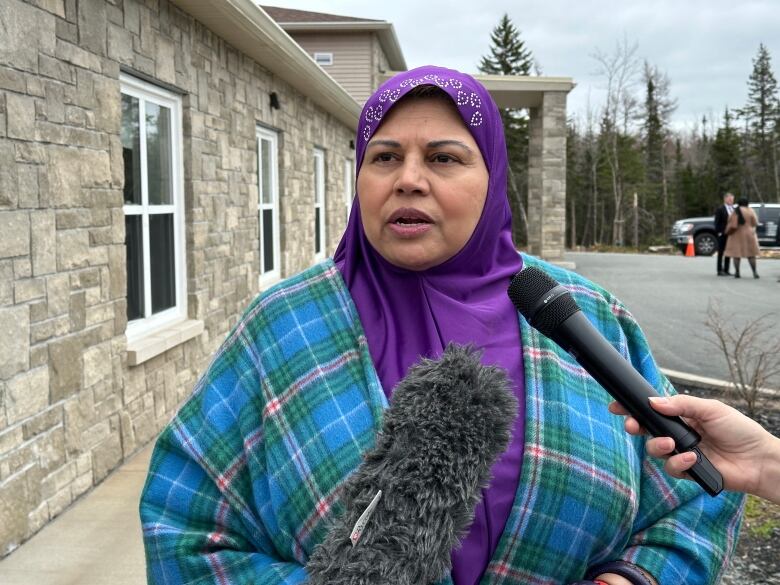 a woman wearing a hijab speaks into two microphones outside of a mosque 