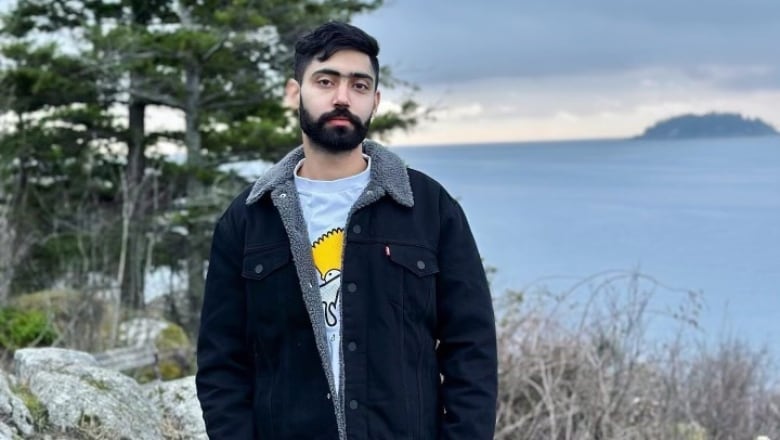 A South Asian man smiles while in a waterfront environment.