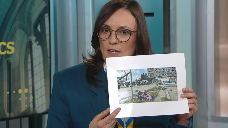 A woman holds up a photo that shows an overturned stroller in the foreground and emergency crews in the background.