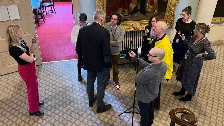 A group of people stand in a hallway pointing recording devices toward a man.