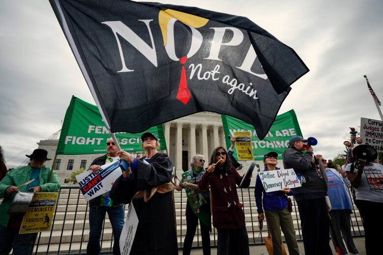 Several people wave big flags and signs at the foot of steps leading to an august building. 