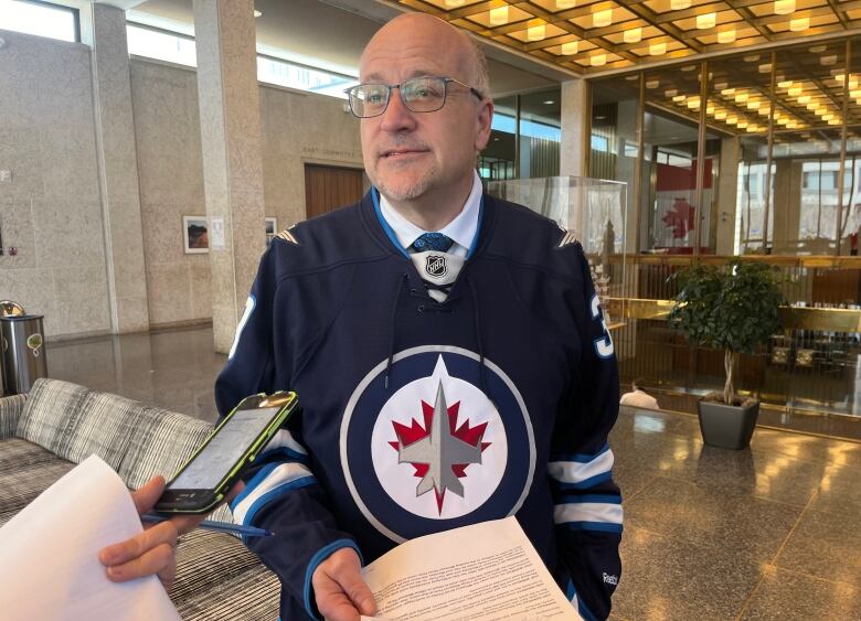 A man wearing a Winnipeg Jets jersey speaks to reporters.