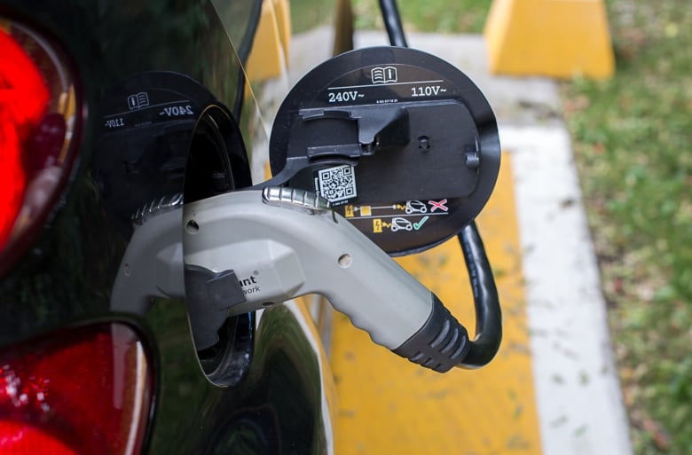 A closeup of the handle of a charging cord plugged into a black car.