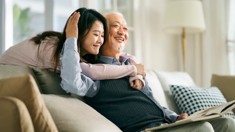 A younger person embraces an older person while they sit on a sofa.