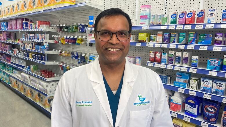 A pharmacist stands in a white coat in front of products. 