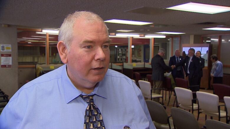 A man in a blue shirt and tie does an interview. 