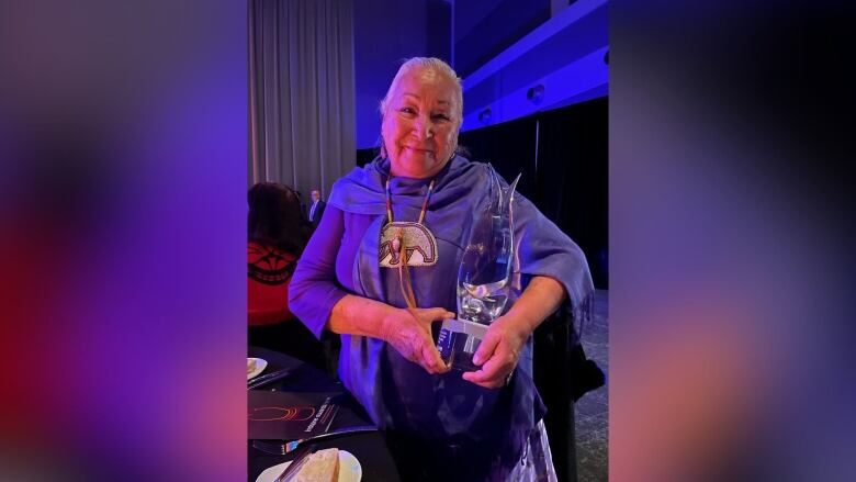 An older woman holding an award made of glass.