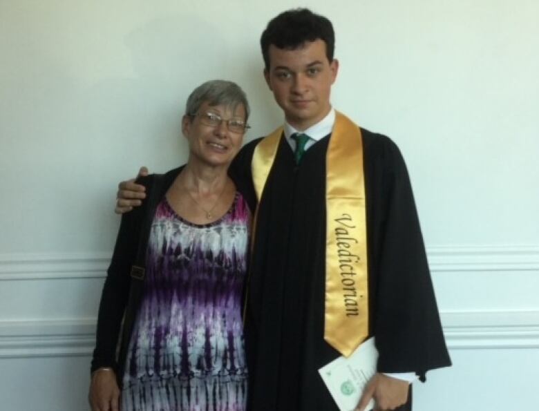 A young person with their mother on graduation day in a robe and Valedictorian sash. 