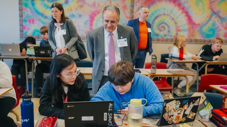 Man stands behind two students 