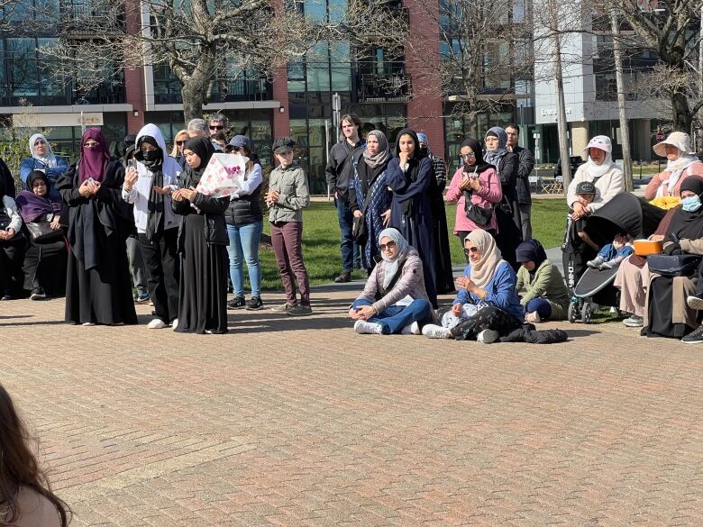 A group of people in a park , many are women wearing Muslim headdresses, engage in prayer.