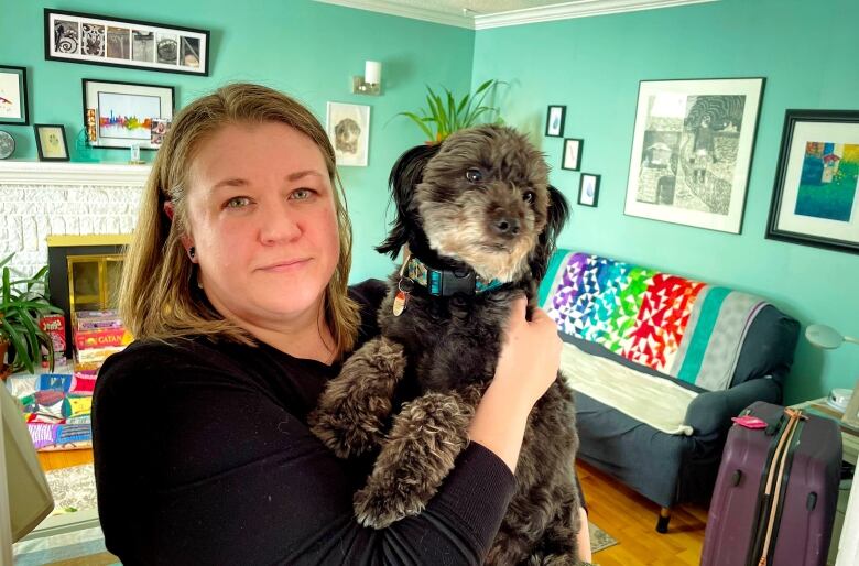 A woman wearing a black shirt holds her grey dog while standing in a living room.