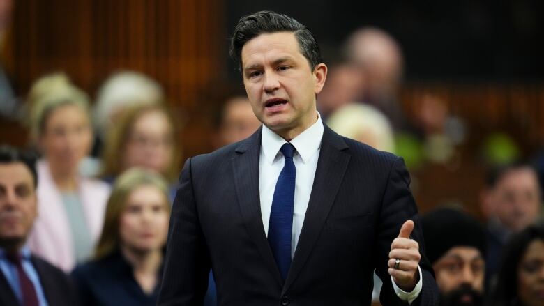 A man in a black suit motions with his hand as he speaks in the House of Commons.