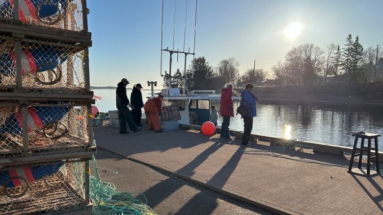 Several people standing around a lobster boat. The sun, low in the sky, is reflected on calm water.