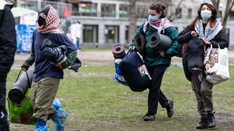 Several people in masks and wearing keffiyehs leave with their belongings from an encampment at McGill University.