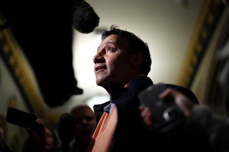 A man speaks to into a number of recording devices being held by reporters.