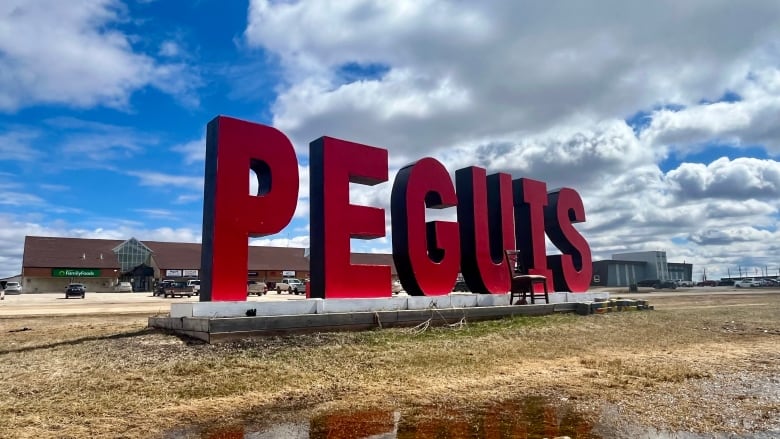 The red Peguis sign in front of the Peguis band office, reflected in a puddle.