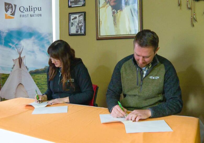 A man and a woman sign a document at a table.