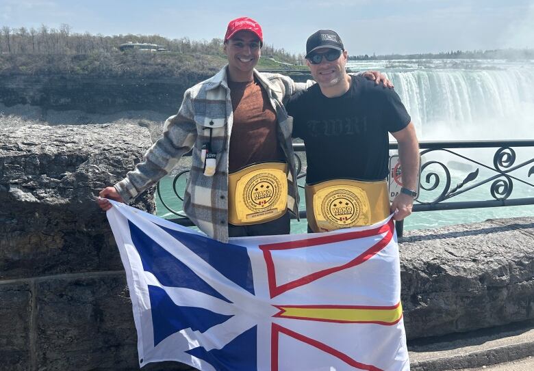 Two men stand side by side holding the Newfoundland flag. Niagara Falls is in the background. 