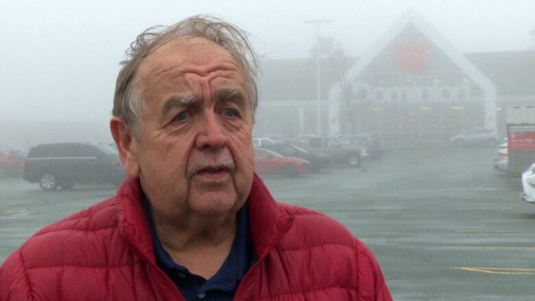 A man wearing a red coat stands outside a Dominion grocery store.