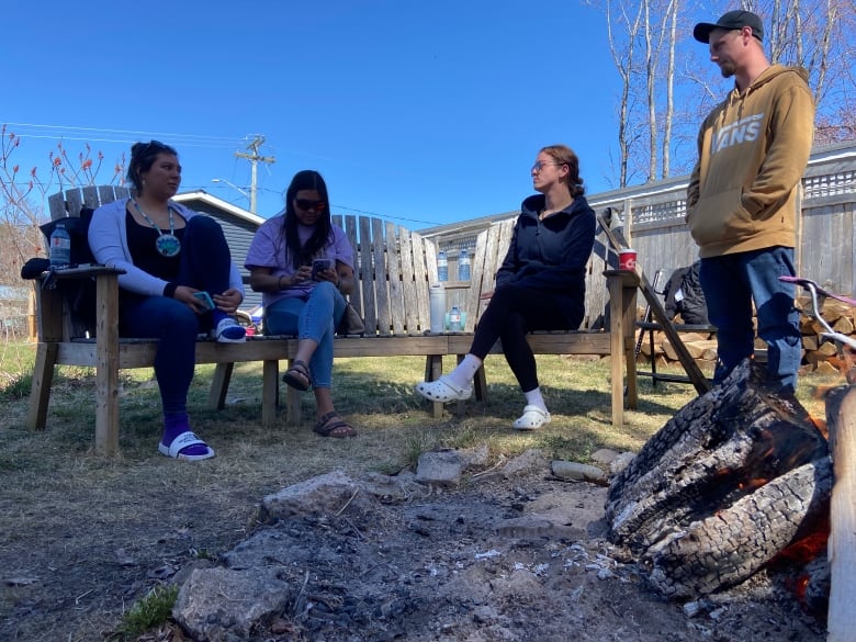 People sit in chairs around a fire outside.