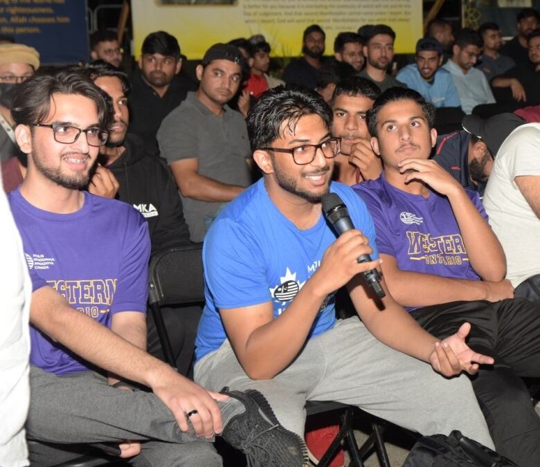 Young South Asian men speak at a religious gathering.