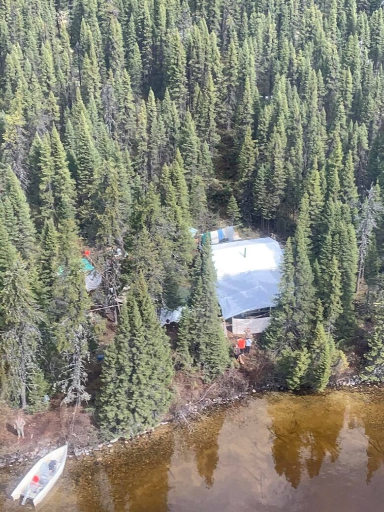 A cabin between trees and a body of water. 