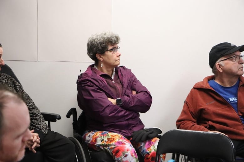 A woman sitting in a wheelchair crosses her arms and looks forward