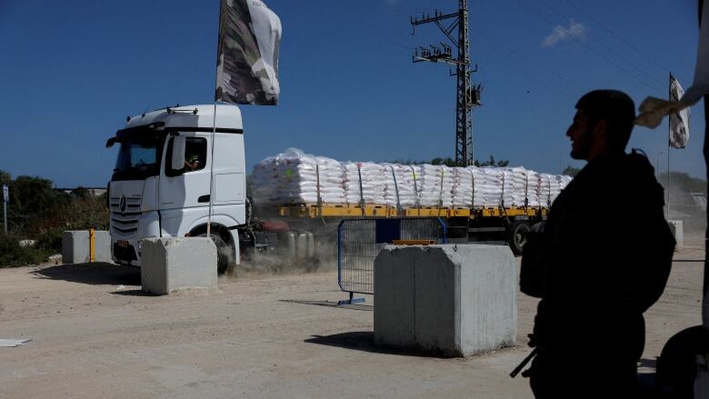 A soldier stands guard as a truck carrying humanitarian aid navigates a checkpoint.