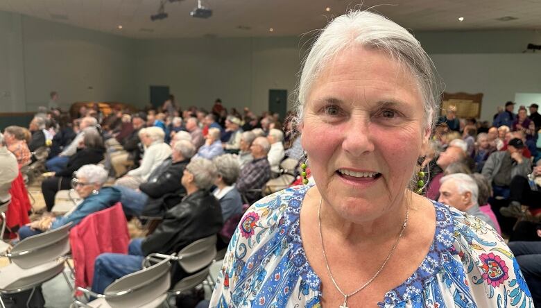 A woman smiles at the camera with an auditorium full of people behind her.